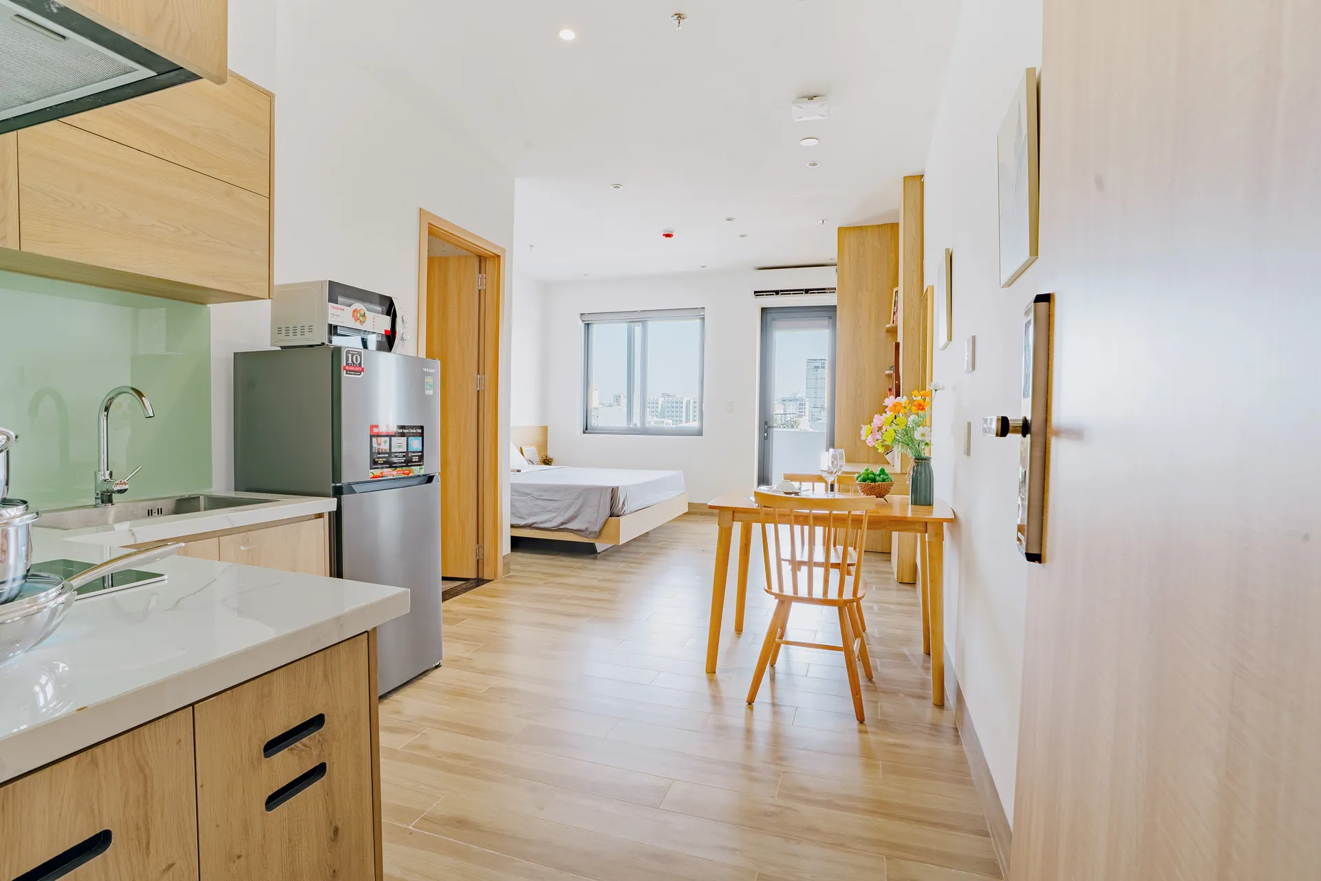 An open-plan studio apartment: kitchen in the foreground, bed and dining table beyond.