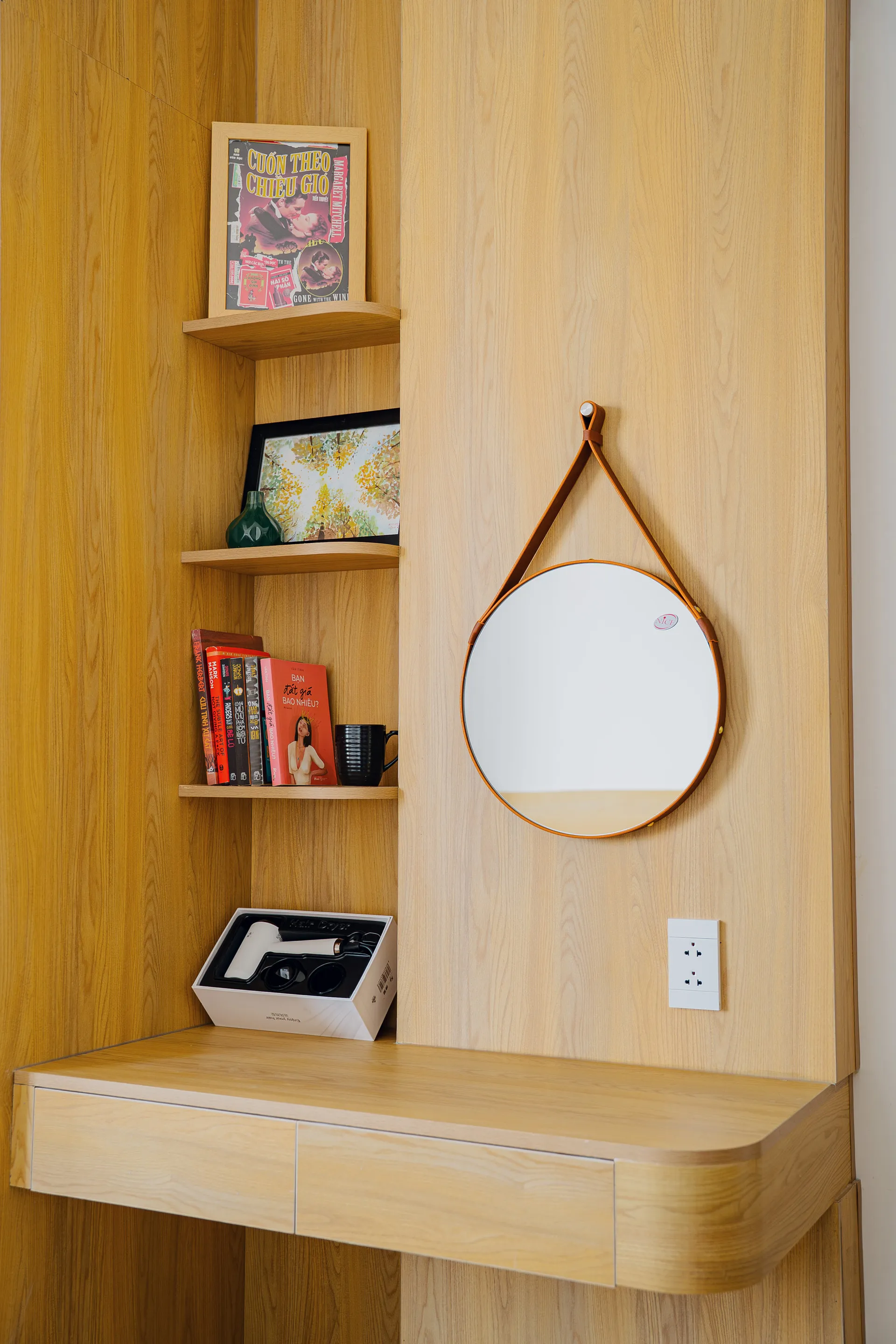 A built-in shelf with books and a round leather-strap mirror.
